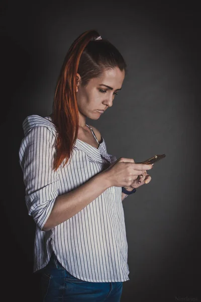 Elinde cep telefonu olan kızıl saçlı bir kız.