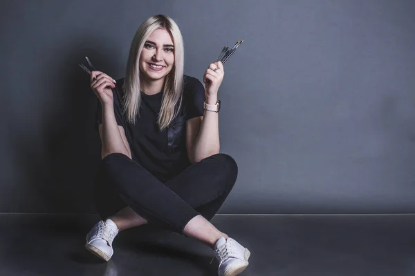 Gri arka planda fırçaları olan sarışın bir kız.