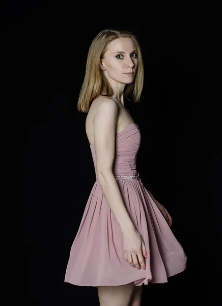 a girl with fair skin and light hair in a short puffy pink dress is spinning and smiling on a black background