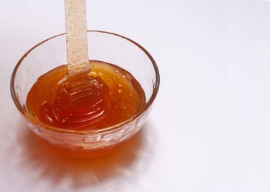 Açık kahverengi bal camdan bir kaseye dökülüyor. Beyaz arka plan. Boşluğu kopyala..
