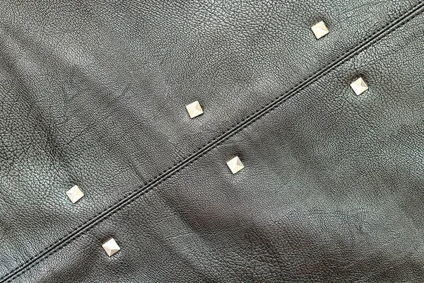 Close-up of black leather material with stitching and metal elements. Fabric texture and background for design and decoration. The concept of making leather goods and clothing.