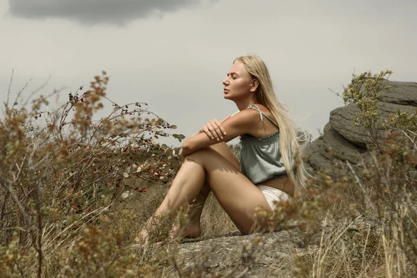 Bir kız ormanın ve gölün ortasında bir kayanın üzerinde oturuyor.