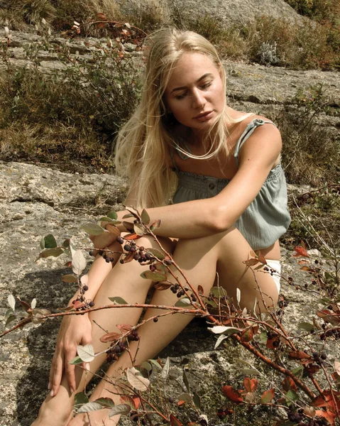 Genç kız bir kayanın üzerinde oturuyor.