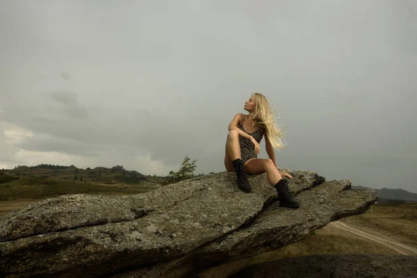 Kadın kayanın üzerinde oturuyor.