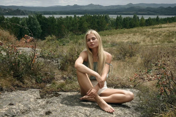 Bir kız ormanın ve gölün ortasında bir kayanın üzerinde oturuyor.