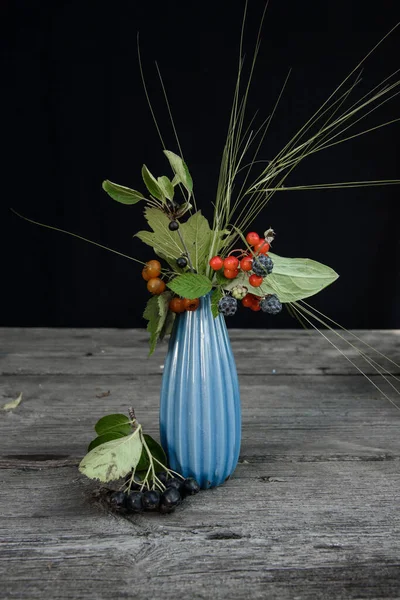 Masanın üzerinde yabanmersini kompozisyonu olan mavi vazo.