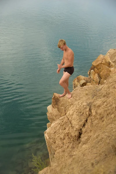 Nastolatek na skalistym brzegu przed kąpielą w błękitnym, czystym jeziorze — Zdjęcie stockowe
