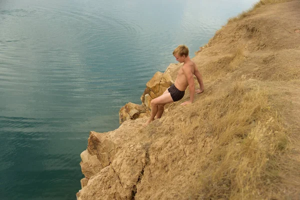 Tiener op rotsachtige kust voor het zwemmen in blauw, helder meer — Stockfoto