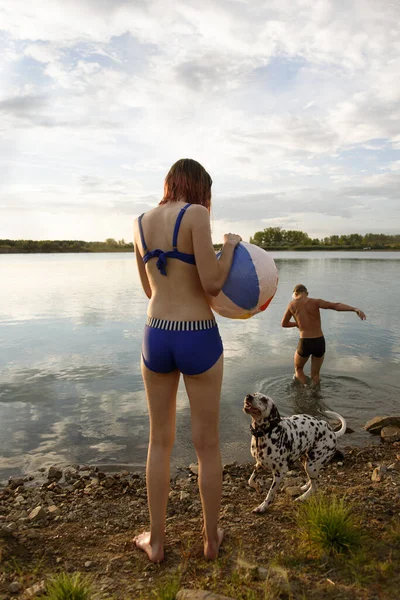 Jong aantrekkelijk meisje speelt bal met hond in blauw meer water. Achteraanzicht. — Stockfoto