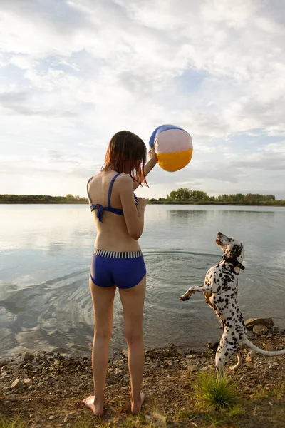 Młoda atrakcyjna dziewczyna gra w piłkę z psem w błękitnej wodzie jeziora — Zdjęcie stockowe