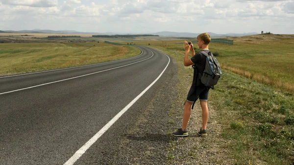 A young man takes pictures on a phone landscape next to a country road — Stock Photo, Image