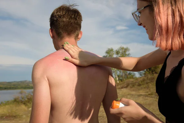 Kız, erkek arkadaşlarına güneş kremi sürüyor.