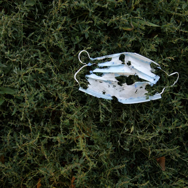 Virüse karşı kişisel koruyucu ekipmanlarla çevre kirliliği. Dışarıdaki çimlerin arasında yerde kullanılmış yüz maskesi. Salgın sonrası çöpler.