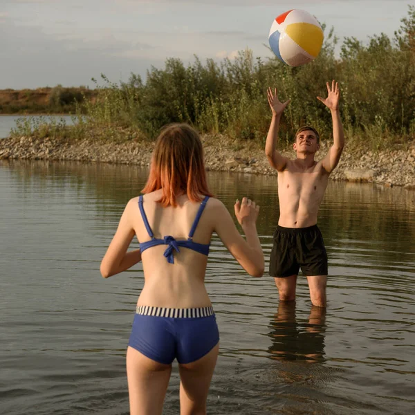 Facet i dziewczyna stoją w jeziorze i grają w nadmuchiwaną piłkę — Zdjęcie stockowe
