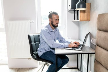 Adam bilgisayarın başına oturur, dizüstü bilgisayara bakar ve e-postaya cevap verir.