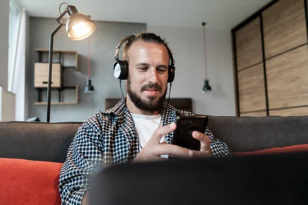 Adam kulaklıkla müzik dinliyor, kanepeye oturuyor ve akıllı telefonuna bir mesaj yazıyor.