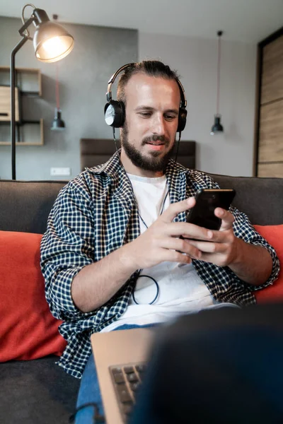 Adam kulaklıkla müzik dinliyor, kanepeye oturuyor ve akıllı telefonuna bir mesaj yazıyor.