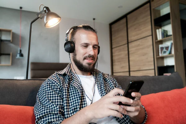 Adam kulaklıkla müzik dinliyor, kanepeye oturuyor ve akıllı telefonuna bir mesaj yazıyor.