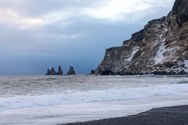 black beach and rocks and waves near the Voyage Vik during the winter sunset