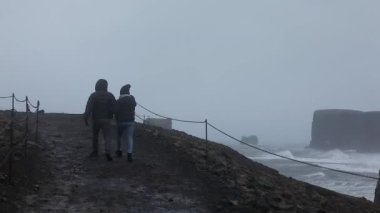 Turistler İzlanda 'daki Burun' da izleri takip ediyor ve güçlü rüzgar fırtınalarıyla mücadele ediyorlar.