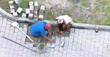 İki işçi yola kaldırım taşı monte ediyor.