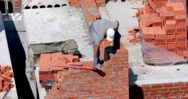 İnşaatçı yüksek bir binanın duvarında duruyor ve çalışma kalitesini kontrol ediyor.