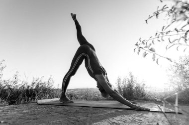 Siyah ve beyaz yaşlı kadın yoga poziyonu alıyor. Beyaz aurora arka planında baş aşağı köpek pozisyonu alıyor.