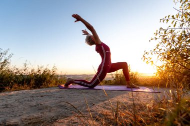 Hilal ay pozu veren emekli kadın gün doğumunda yoga yapıyor.