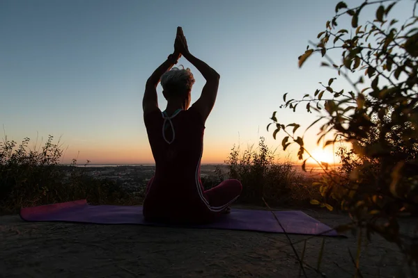 Dark photo Woman back view holding hands up while sitting in lotus position on morning sunrise and town background