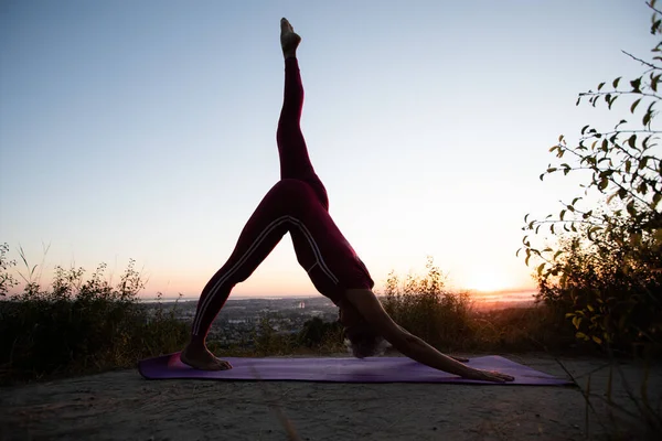 Aşağıya bakan köpek pozu veren kadın, sabah gün doğumunda yoga yapıyor.