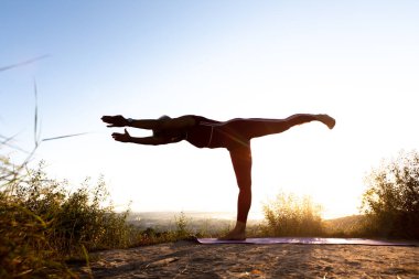 Kırmızı eşofmanlı, gölgeli yaşlı bir kadın yoga yapıyor spor spreyinde denge çubuğu kullanıyor.