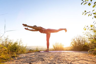 Kırmızı eşofmanlı yaşlı kadın güneş doğarken yoga yapıyor spor spreyinde denge çubuğu kullanıyor.
