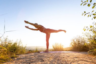 Gün doğumunda yoga egzersizi yapan iki el spor minderinin üstünde denge çubuğu yapmaya çalışan bir kız.