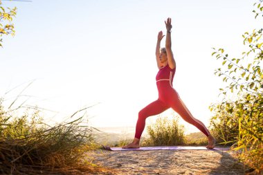 Gün doğumunda yoga yapan bir kız iki elini spor minderinin üstüne koyuyor.