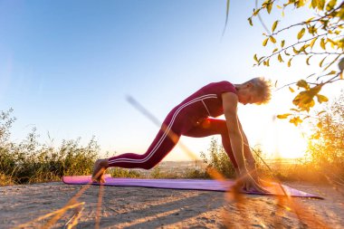 Kırmızı eşofmanlı yaşlı kadın Baddha Trikonasana 'yı yapıyor Bir el aşağı Poz verdi