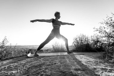 Kırmızı pantolonlu, siyah ve beyaz yaşlı kadın yoga pozisyonu yapıyor. Savaşçı Virabhadrasana 'yı gölgelerde keşfet.