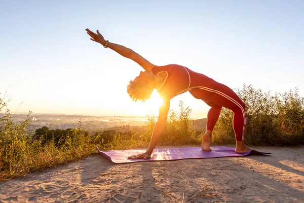 Woman doing Wheel half Moon power Pose lift up one hand in the sunrise