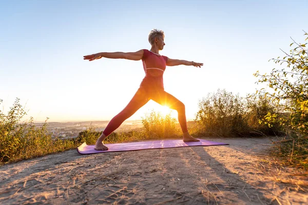 Kırmızı pantolonlu kadın yoga pozisyonunda Savaşçı Virabhadrasana 'yı keşfediyor.
