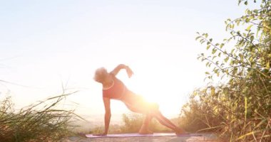 Kadın gün doğumunda yoga germe ve bükme egzersizleri yapıyor.