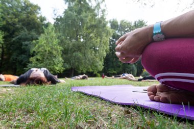 Saat ve el Kadın Yoga Ustası, Park 'ta yerde yatan bir grup insanla Hatha Töreni düzenliyor.