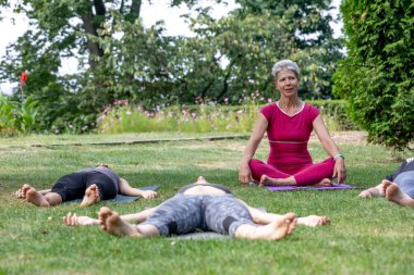 Yoga ustası Hatha seremonisi düzenliyor. Bir grup insan parkta yerde yatıyor.