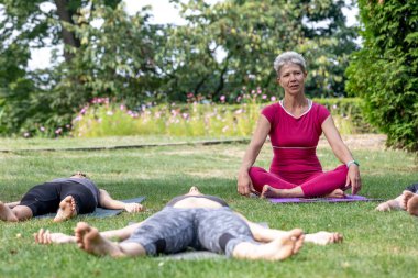 Yoga ustası Hatha seremonisi düzenliyor. Bir grup insan parkta yerde yatıyor.