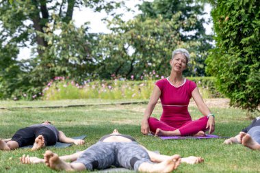 Yoga ustası Hatha seremonisi düzenliyor. Bir grup insan parkta yerde yatıyor.