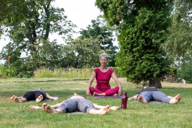 Yoga ustası Hatha seremonisi düzenliyor. Bir grup insan parkta yerde yatıyor.