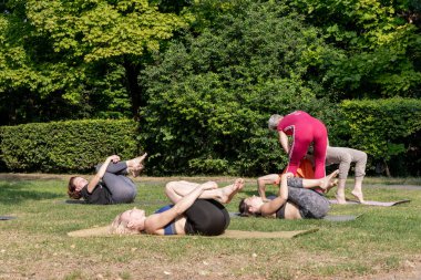 Kadın yoga ustası gruba kasları germek için dizlerinin üzerine çöküp poz vermelerine yardım ediyor.