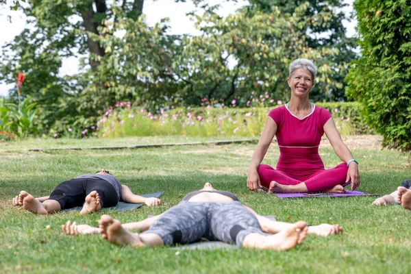 Yoga ustası Hatha seremonisi düzenliyor. Bir grup insan parkta yerde yatıyor.