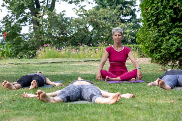 Yoga ustası Hatha seremonisi düzenliyor. Bir grup insan parkta yerde yatıyor.