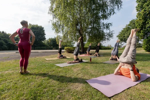 Kadın yoga ustası grubu kurmak istiyor. Omuzlar dışarıda parkta poz veriyor.