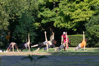 Kadın yoga ustası parkta Yan Plank pozu vermesine yardım ediyor.