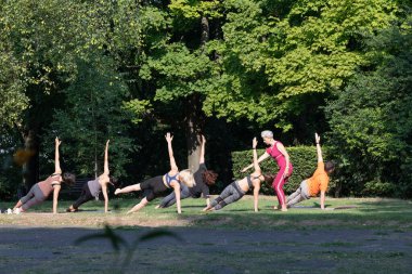 Kadın yoga ustası, parkta Yan Plank pozu vermek için grubu denetliyor.